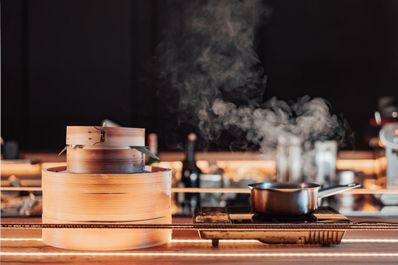 A close-up of a bamboo steamer and saucepan emitting steam in a kitchen setting, showcasing cooking ambiance.